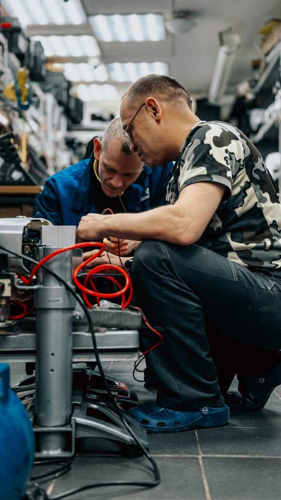 Two technicians focusing on equipment repair in a busy workshop setting.